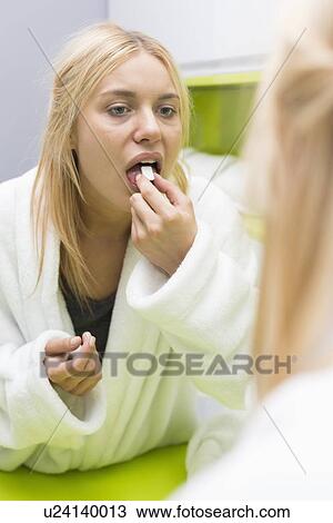 Young woman taking medicine while looking at mirror View Large Photo Image Stock Image - Young woman taking medicine while looking at mirror. Fotosearch