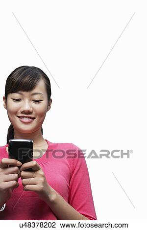 Stock Image - Young woman text messaging on cell phone against white background. Fotosearch