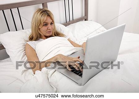 Young woman using laptop in bed View Large Photo Image Picture - Young woman using laptop in bed. Fotosearch
