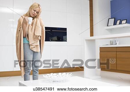 Young woman wrapped in blanket holding coffee mug while suffering from headache in house View Large Photo Image Stock Image - Young woman wrapped in blanket holding coffee mug while suffering from headache in house. Fotosearch