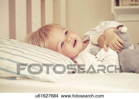 Picture - Baby girl lying in bed. Fotosearch