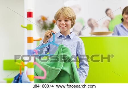 Picture - Boy hanging hooded top on coat hook. Fotosearch