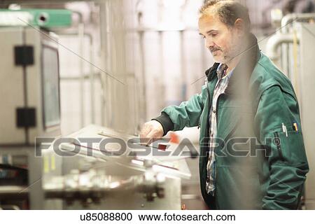 Stock Image - Brewery worker operating machine. Fotosearch