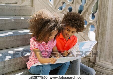 Stock Image - Brother and sister on steps looking at map. Fotosearch