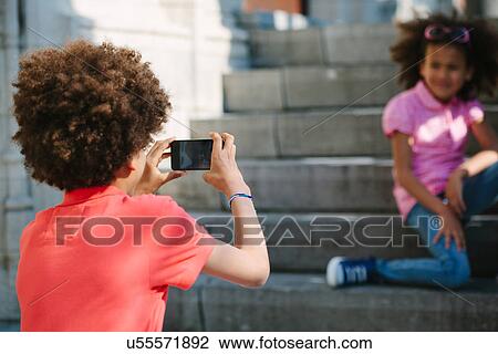 Stock Image - Brother taking photograph of sister on stairway. Fotosearch