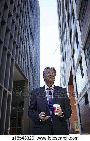 Businessman holding smartphone and hot drink View Large Photo Image Stock Photo - Businessman holding smartphone and hot drink. Fotosearch