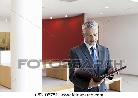Stock Image - Businessman in waiting area of office, looking at paperwork. Fotosearch