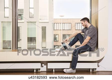 Businessman sitting on windowsill using laptop View Large Photo Image Stock Image - Businessman sitting on windowsill using laptop. Fotosearch