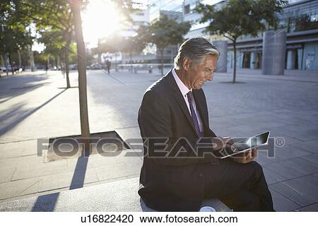 Stock Image - Businessman sitting outside using digital tablet. Fotosearch