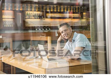 Stock Photograph - Businessman using laptop, view through window. Fotosearch