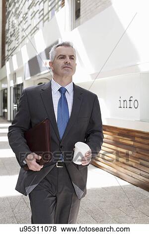 Businessman walking down corridor in office View Large Photo Image Stock Photo - Businessman walking down corridor in office. Fotosearch