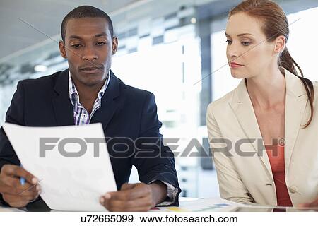 Businesspeople sitting at desk, looking at paperwork View Large Photo Image Stock Photo - Businesspeople sitting at desk, looking at paperwork. Fotosearch