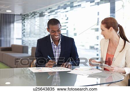 Businesspeople sitting at desk, looking at paperwork View Large Photo Image Stock Photography - Businesspeople sitting at desk, looking at paperwork. Fotosearch