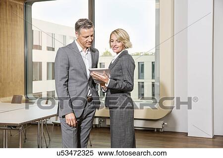 Stock Photography - Businesspeople standing in conference room, using digital tablet. Fotosearch