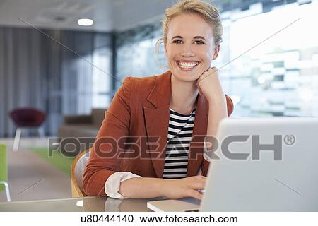Businesswoman sitting at desk, using laptop View Large Photo Image Stock Image - Businesswoman sitting at desk, using laptop. Fotosearch