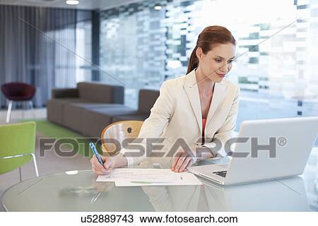 Stock Image - Businesswoman sitting at desk, writing activity. Fotosearch