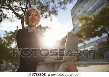 Businesswoman sitting outside using laptop View Large Photo Image Stock Photo - Businesswoman sitting outside using laptop. Fotosearch