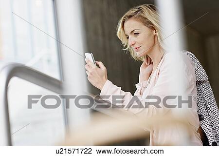 Stock Image - Businesswoman using mobile phone in office building. Fotosearch