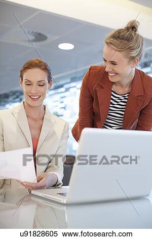 Businesswomen sitting at desk, using laptop View Large Photo Image Stock Photography - Businesswomen sitting at desk, using laptop. Fotosearch