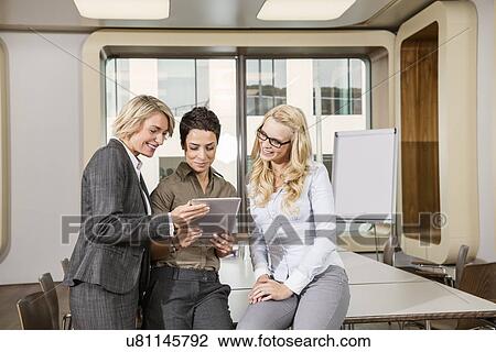Stock Image - Businesswomen sitting on conference table looking at digital tablet. Fotosearch