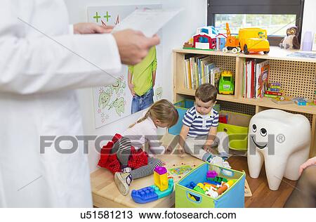 Stock Image - Children playing on floor, dentist in foreground. Fotosearch