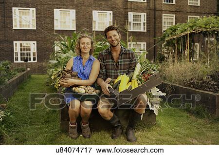 Stock Photo - Couple holding harvested vegetables on council estate allotment. Fotosearch