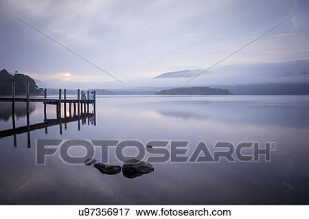 Couple on pier by tranquil lake, Cumbria, England, UK View Large Photo Image Stock Photo - Couple on pier by tranquil lake, Cumbria, England, UK. Fotosearch