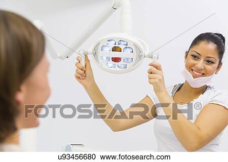 Stock Image - Dental nurse adjusting lights in dentists. Fotosearch