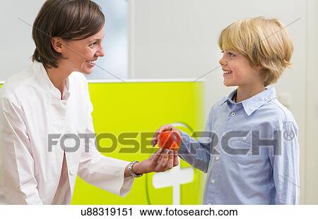 Dentist giving boy apple in dental reception View Large Photo Image Stock Image - Dentist giving boy apple in dental reception. Fotosearch