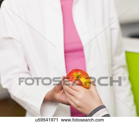 Stock Image - Dentist giving girl apple, close up. Fotosearch