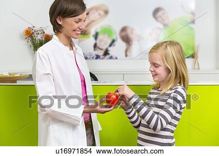 Picture - Dentist giving girl apple in dental reception. Fotosearch