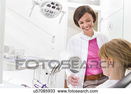 Dentist holding hand mirror in front of girls face View Large Photo Image Stock Image - Dentist holding hand mirror in front of girls face. Fotosearch