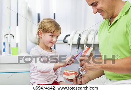 Stock Image - Dentist teaching girl how to brush teeth. Fotosearch