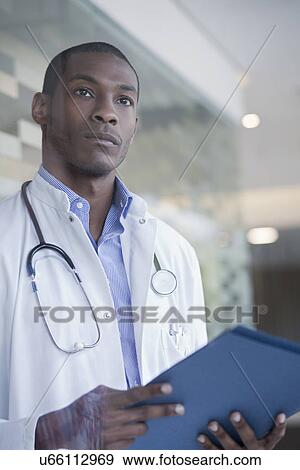 Stock Photo - Doctor standing in hospital corridor holding paperwork. Fotosearch
