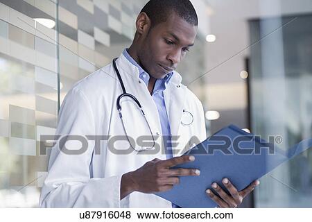 Doctor standing in hospital corridor holding paperwork View Large Photo Image Stock Photo - Doctor standing in hospital corridor holding paperwork. Fotosearch