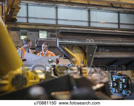 Stock Image - Engineers inspecting engineering drawings together in factory. Fotosearch