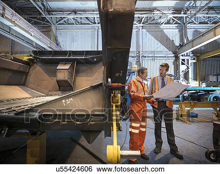 Stock Photograph - Engineers inspecting engineering drawings in factory. Fotosearch
