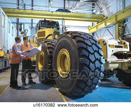 Stock Image - Engineers with engineering drawings inspecting heavy truck. Fotosearch