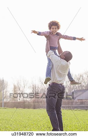 Stock Image - Father lifting up son in field. Fotosearch