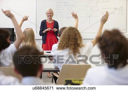 Stock Image - Female teacher and class with hands raised. Fotosearch