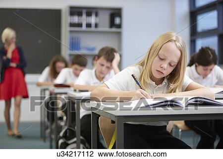 Stock Image - Female teacher watching class doing educational exam. Fotosearch