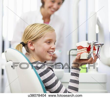 Picture - Girl in dentists chair holding false teeth. Fotosearch