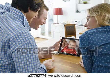 Grandmother and adult grandchildren looking at photo of baby boy on digital tablet View Large Photo Image Picture - Grandmother and adult grandchildren looking at photo of baby boy on digital tablet. Fotosearch