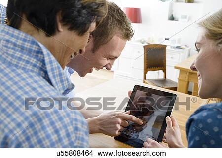 Picture - Grandmother and adult grandchildren using distortion on digital tablet. Fotosearch