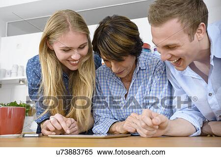Stock Photography - Grandmother looking at digital with adult grandchildren. Fotosearch