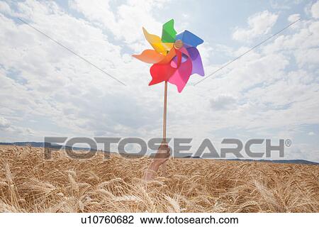Stock Image - Hand holding windmill in wheat field. Fotosearch