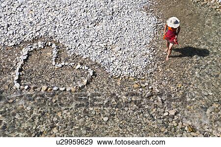 Stock Photo - High angle view of woman walking in river and stones in heart shape. Fotosearch