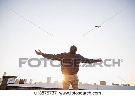 Stock Photo - Man on rooftop with arms outstretched. Fotosearch