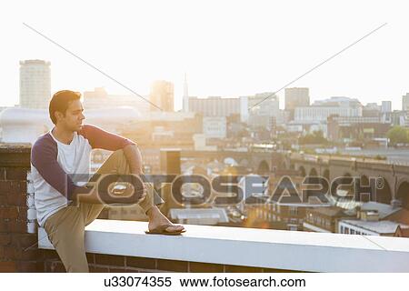 Stock Photography - Man sitting on wall on rooftop, Birmingham, England, UK. Fotosearch