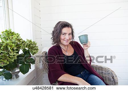 Stock Image - Mature woman having coffee break in conservatory. Fotosearch